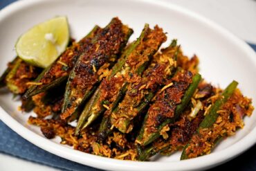 Plated Bharela Bhinda with sev, garnished with lime wedges.