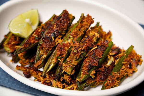 Plated Bharela Bhinda with sev, garnished with lime wedges.