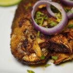 Close-up of Pomfret Fish Fry, highlighting the golden crust and fresh onion slices.