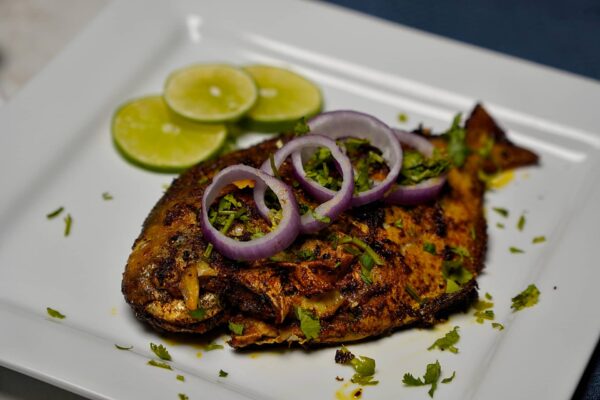 Crispy Pomfret Fish Fry garnished with sliced onions on a white plate.