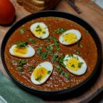 Overhead view of a bowl of spicy egg curry garnished with coriander leaves.