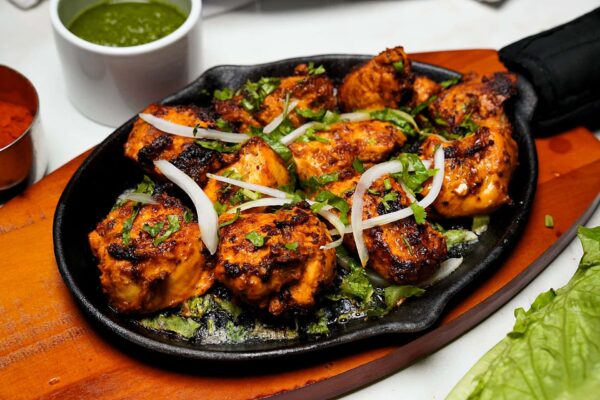 Delicious Chicken Tikka Sizzler served on a hot platter with marinated chicken, sliced onions, and lettuce.