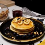 Tall stack of fluffy eggless pancakes drizzled with maple syrup and topped with fresh berries.