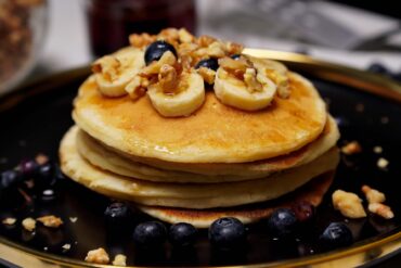 Plate of eggless pancakes topped with banana, walnuts and served with blueberries.