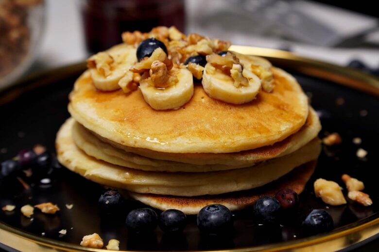 Plate of eggless pancakes topped with banana, walnuts and served with blueberries.
