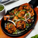Serving Chicken Tikka Sizzler on a sizzling plate, garnished with fresh coriander and accompanied by mint chutney.
