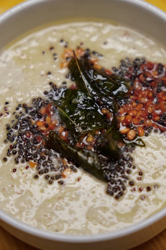 Macro shot of the tempering on coconut chutney, showing the detail of popped mustard seeds, golden urad dal, and glossy green curry leaves.
