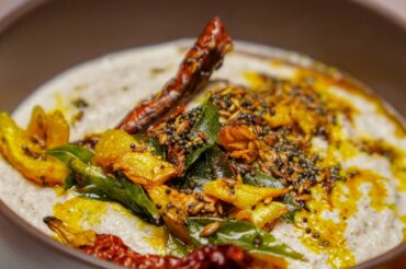 A macro shot of peanut chutney garnished with a vibrant tempering (tadka) of mustard seeds, cumin, dried red chilies, and fresh curry leaves.