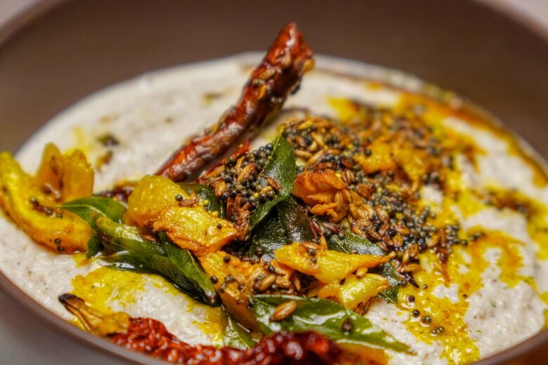 A macro shot of peanut chutney garnished with a vibrant tempering (tadka) of mustard seeds, cumin, dried red chilies, and fresh curry leaves.