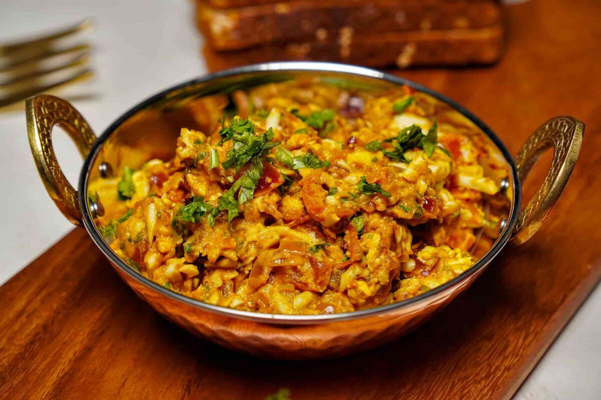 A medium shot of spicy Egg Kheema Masala in a white bowl, garnished with chopped green onions and served on a wooden board.