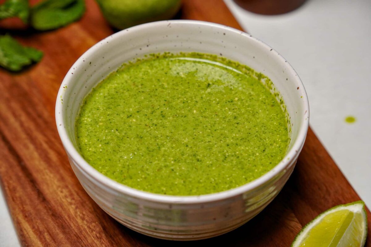 A white ceramic bowl of smooth green coriander chutney with Vibrant texture