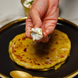 An angled side view of Moong Dal Parathas in a white bowl on a rustic wooden board, showing the soft, flaky texture of the flatbread.