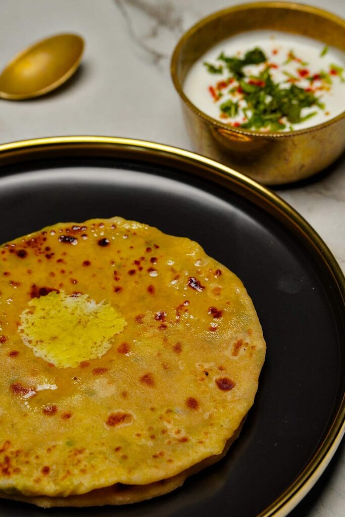 A top-down view of a bowl of Moong Dal Parathas, showing the uniform round shape and vibrant green garnish.