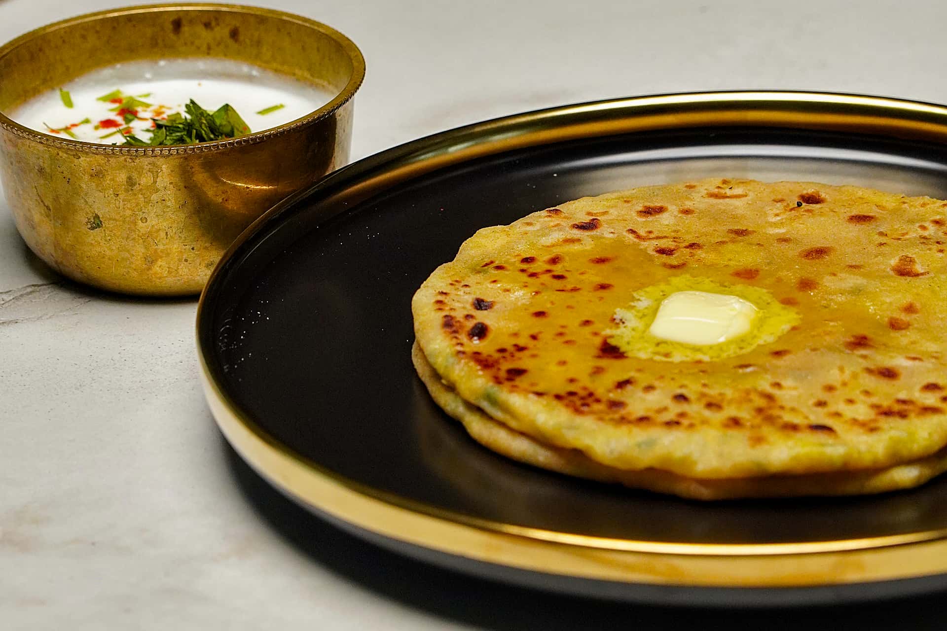 A medium shot of a stack of golden-brown Moong Dal Parathas in a white bowl, garnished with chopped scallions and served on a wooden board.