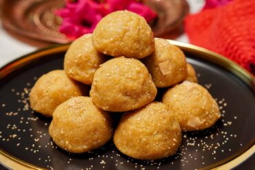 A medium shot of a thaal filled with golden-brown Sooji Jaggery Laddus, garnished with poppy seed served.
