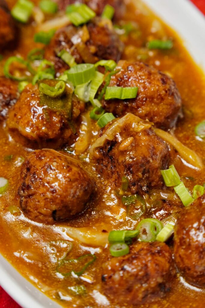 Close-up of double-fried vegetable manchurian balls coated in a thick, shimmering Schezwan and soy-based gravy.