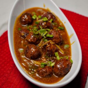 A serving of spicy vegetable manchurian in gravy, garnished with chopped spring onions.