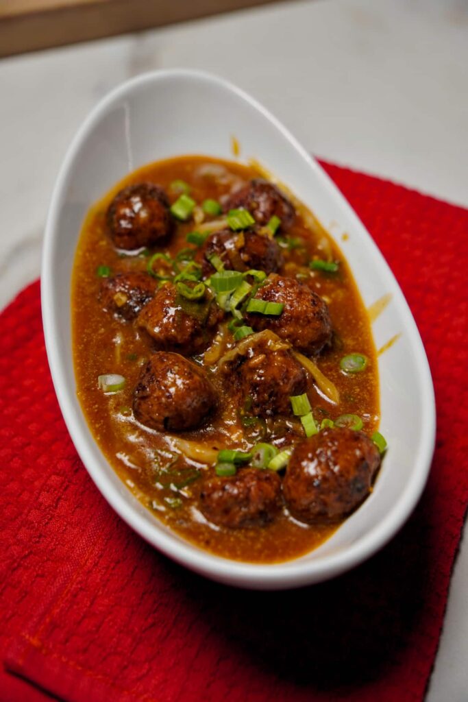 A serving of spicy vegetable manchurian in gravy, garnished with chopped spring onions.