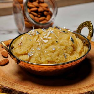 An eye-level side view of Badam Halwa served in a traditional bowl, showing the thick, grainy texture and almond garnishes.