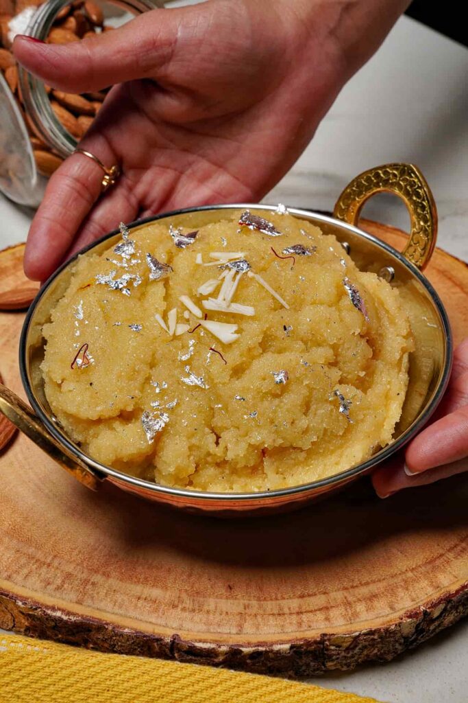 A top-down view of a bowl of Badam Halwa, showcasing the vibrant yellow color and fresh garnishes.