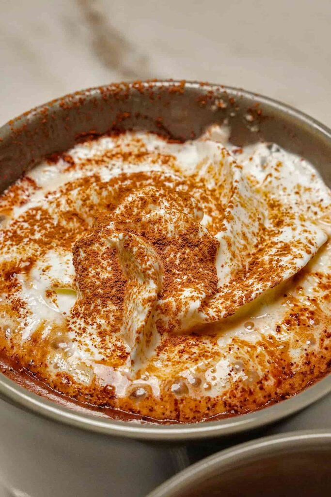 An extreme close-up showing the glossy, velvety texture of melted dark chocolate with whipping cream in a mug