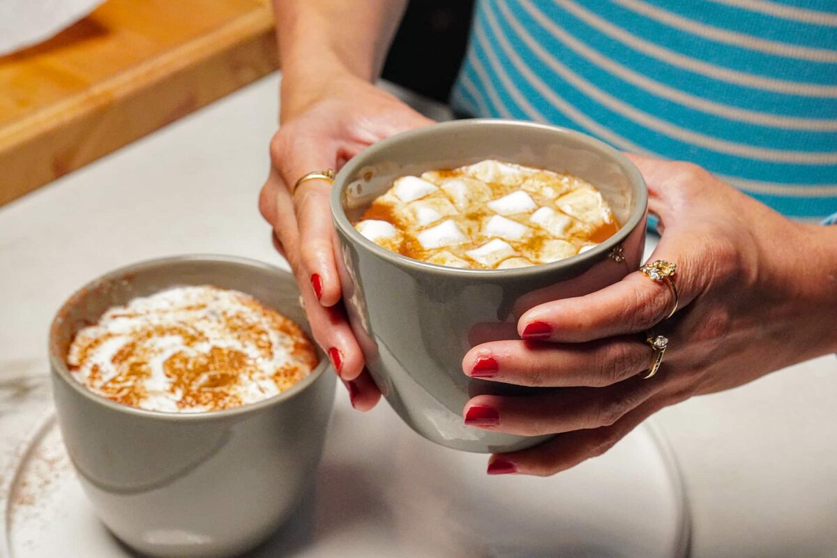 An eye-level view of a mug of thick dark hot chocolate hold in hand