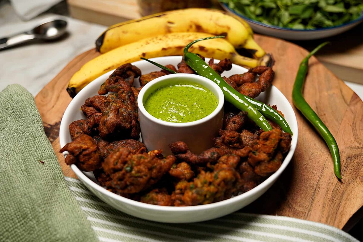 Kela Methi Na Bhajiya served on a plate with fresh bananas, methi leaves, and green chutney in the background.