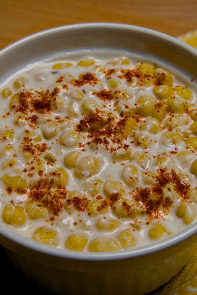 An extreme close-up of Boondi Raita, highlighting the soft texture of soaked boondi mixed with seasoned yogurt and red chili.