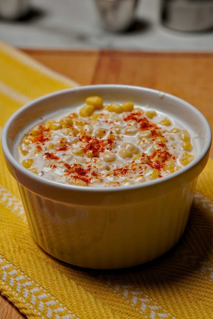 An eye-level side view of Boondi Raita served in a white bowl, showing the thick yogurt base and crunchy boondi garnish.