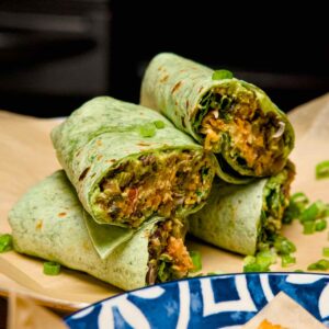 A vertical stack of sliced green breakfast burritos with a side of golden crispy tater tots and garnished with green onions.