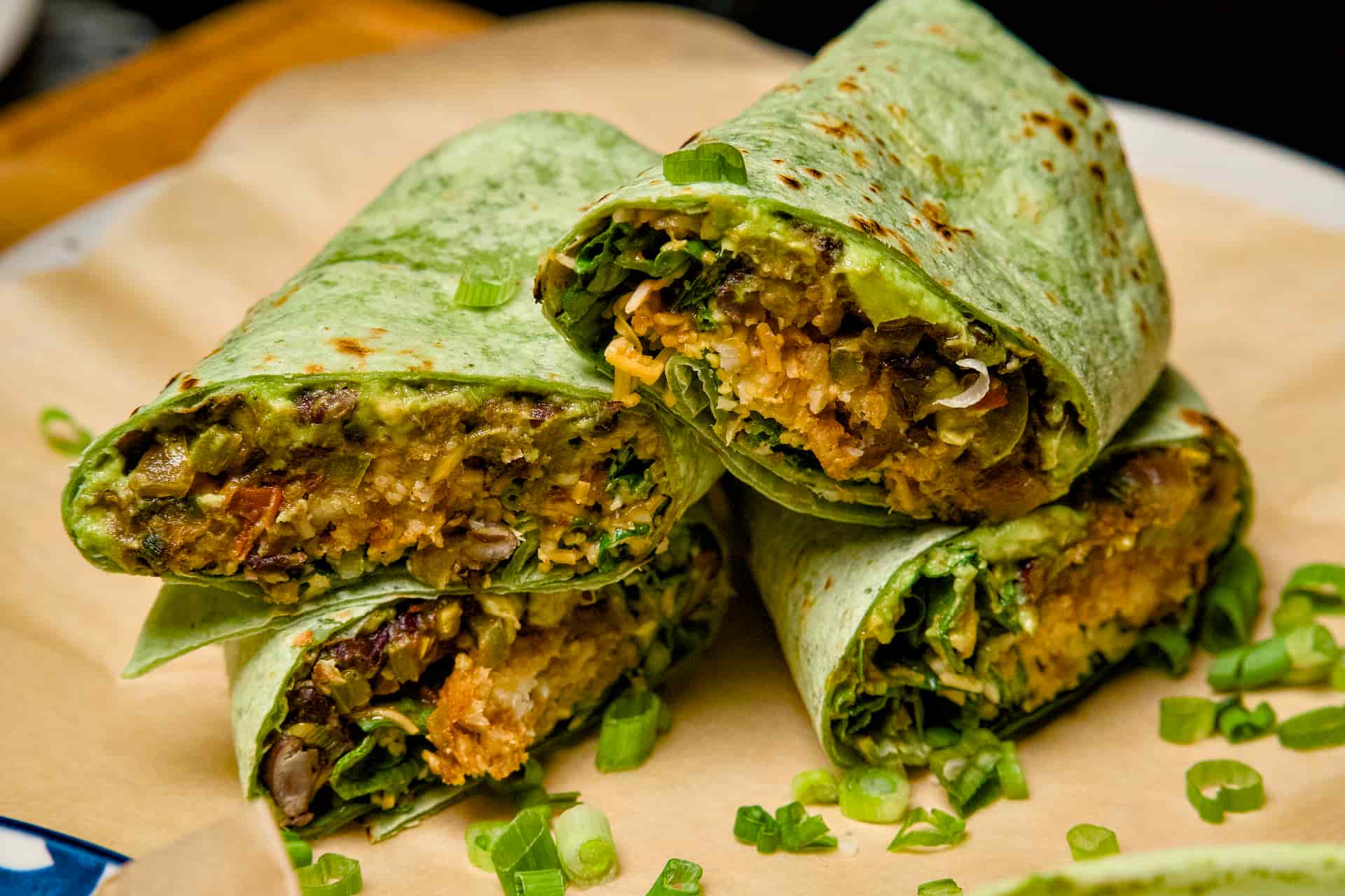 A close-up stack of sliced vegetarian breakfast burritos in green spinach wraps, showing fillings of tater tots, beans, and cheese.