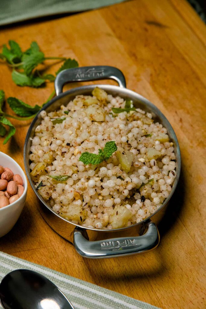 A top-down view of a bowl of Sabudana Khichdi, showcasing the even distribution of peanuts, spices, and green garnishes.