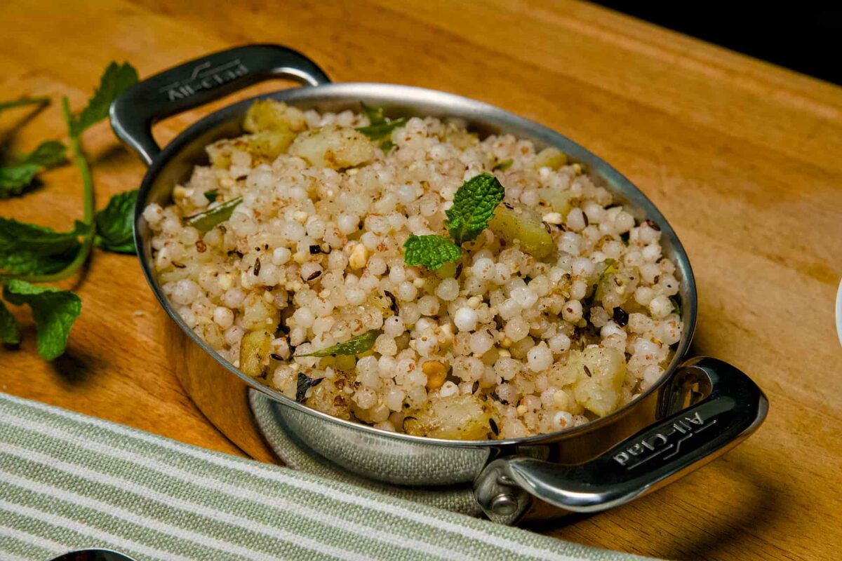 A wide shot of a bowl filled with non-sticky Sabudana Khichdi, garnished with fresh mint and served on a wooden board.