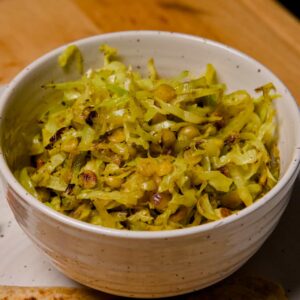 A close-up view of a white ceramic bowl filled with sautéed cabbage and yellow chana dal lentils.