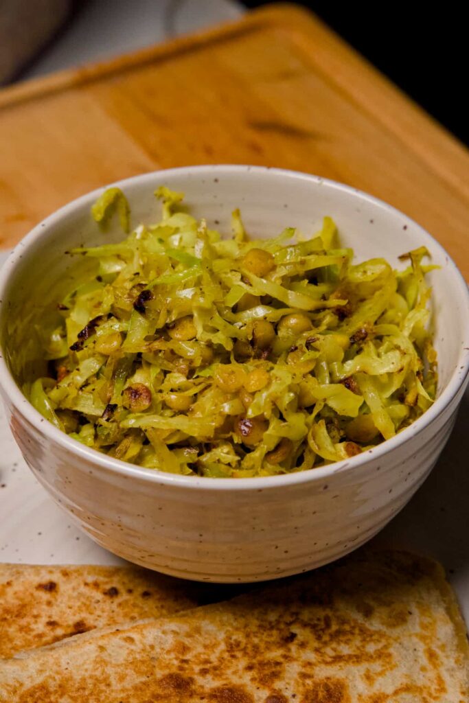 A close-up view of a white ceramic bowl filled with sautéed cabbage and yellow chana dal lentils.