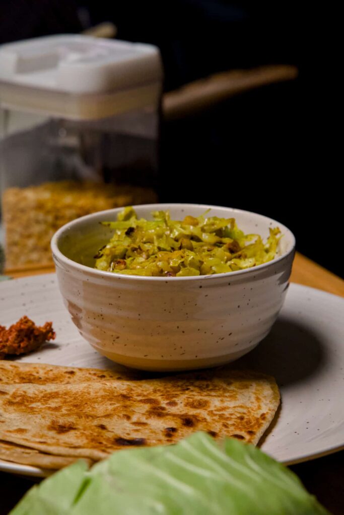 Side angle view of a bowl of cabbage and lentil stir-fry served with flatbread on a large speckled plate.
