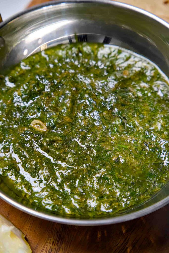 An extreme close-up of the thick, savory texture of dill curry (Suva ni Bhaji) showing the finely chopped dill leaves and garlic pieces in a smooth besan base.