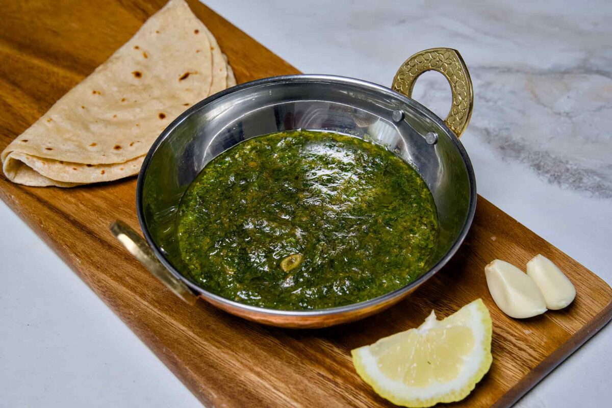 A wide-angle view of a bowl of Suva ni Bhaji alongside fresh chapati and ingredients on a wooden platter, ready to be served as a healthy Indian dinner.