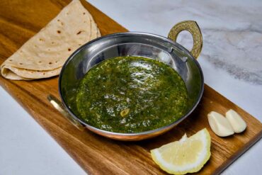 A wide-angle view of a bowl of Suva ni Bhaji alongside fresh chapati and ingredients on a wooden platter, ready to be served as a healthy Indian dinner.