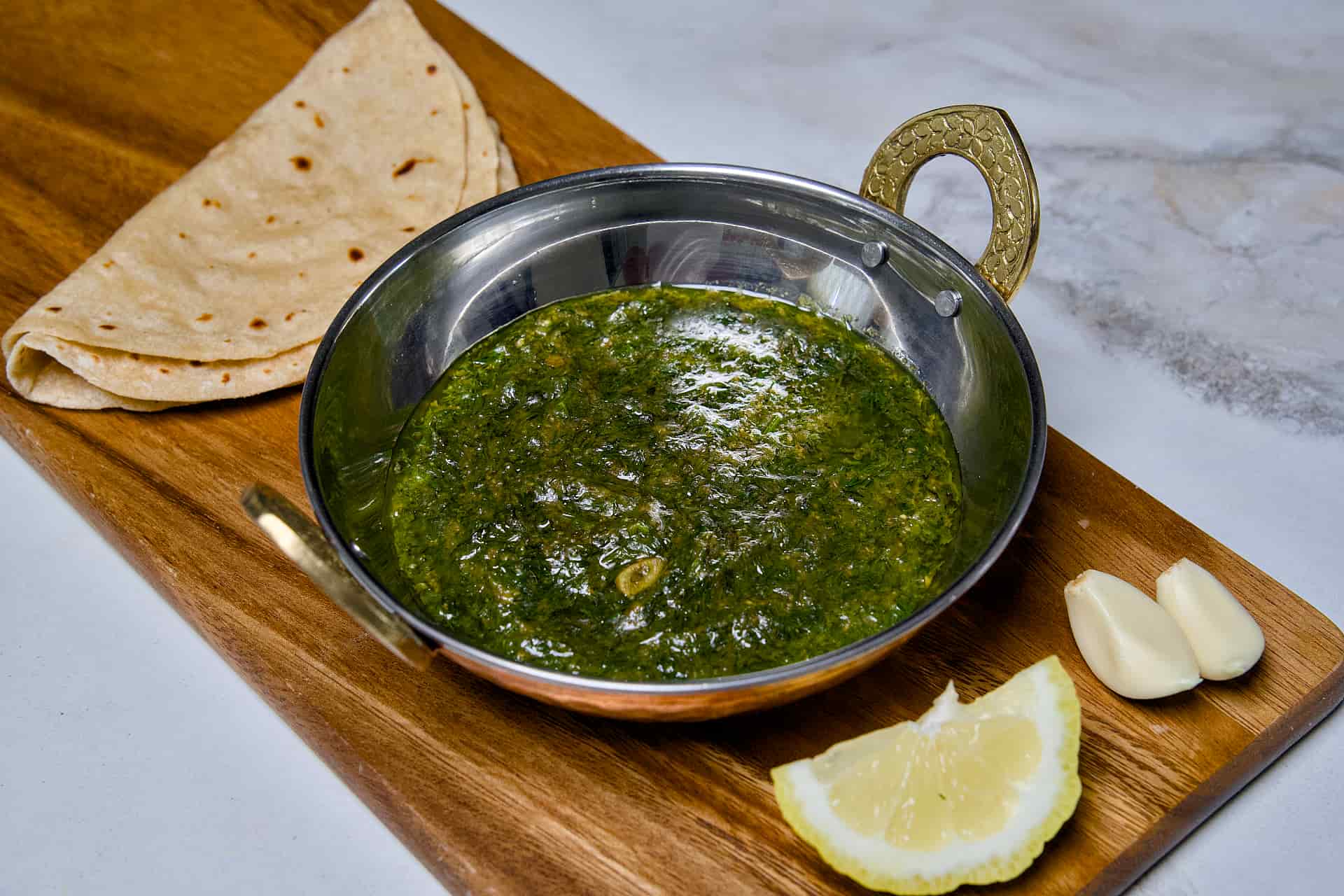 A wide-angle view of a bowl of Suva ni Bhaji alongside fresh chapati and ingredients on a wooden platter, ready to be served as a healthy Indian dinner.
