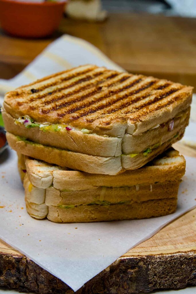 A whole, unsliced triple-decker Bombay sandwich showing perfectly charred golden-brown grill marks from a panini press.