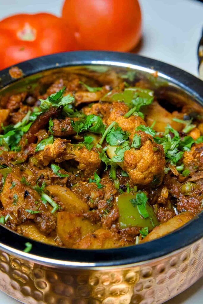 An extreme close-up of Aloo Gobi showing the texture of the sautéed cauliflower florets, green bell peppers, and the rich masala coating.