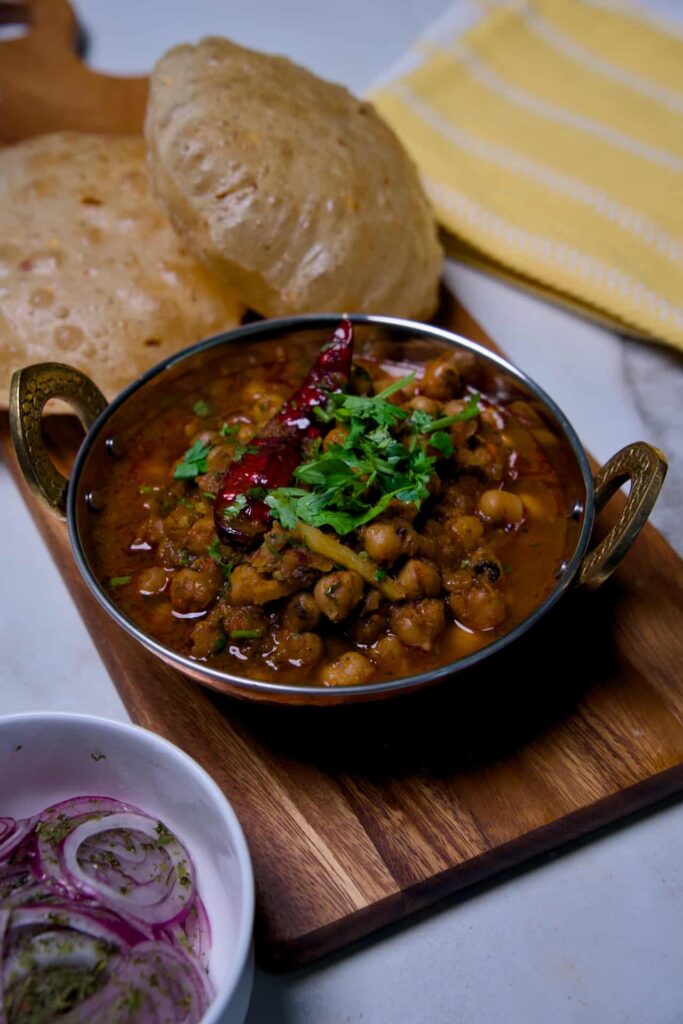 Dhaba style chole masala garnished with fresh coriander leaves and a whole red chili in a traditional brass handle copper dish.